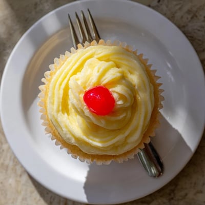 Moist pineapple-infused Dole Whip Cupcakes swirled with creamy yellow frosting on a white plate